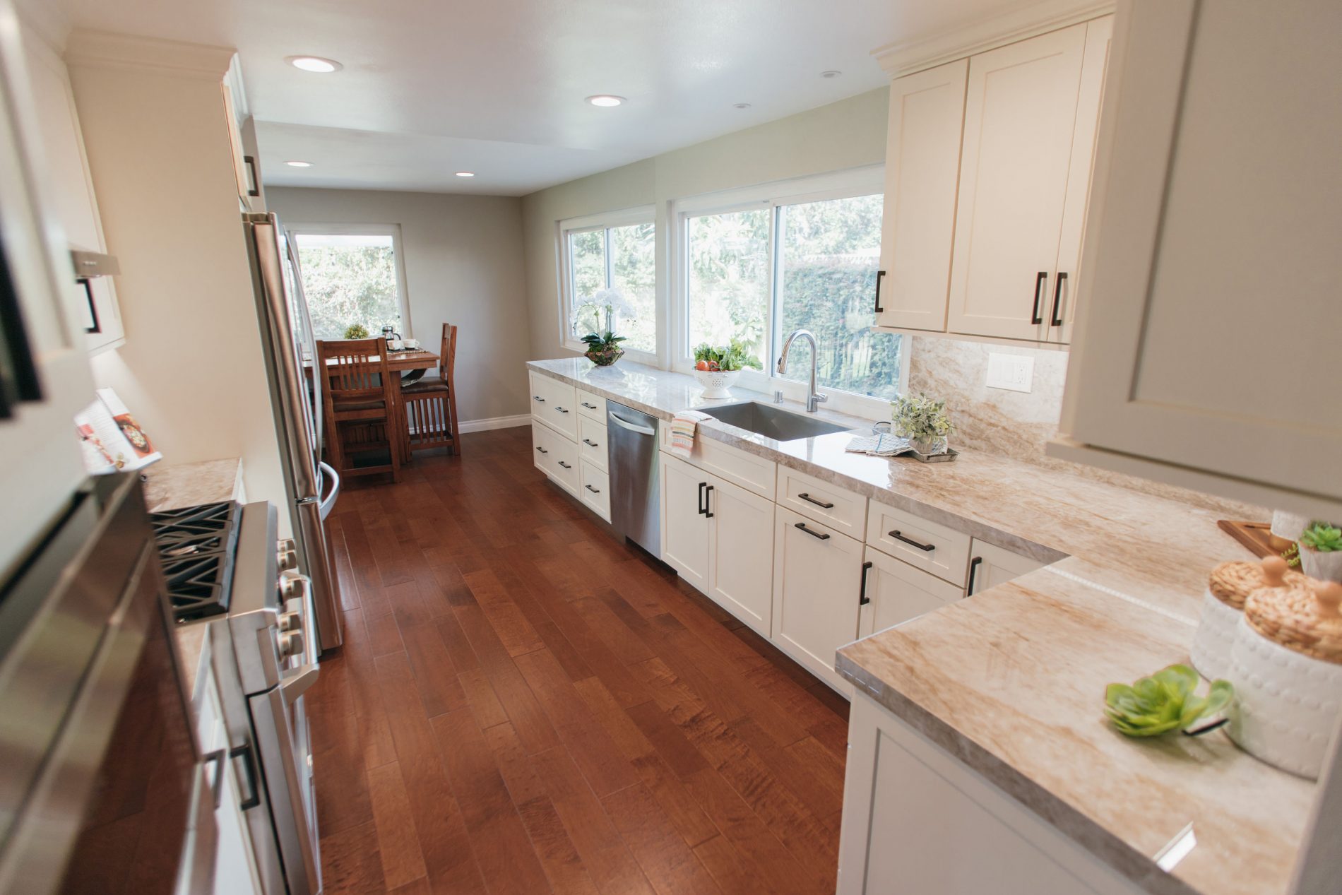 Seneca contemporary galley kitchen with white cabinets, stone counter and backsplash, stainless appliances, wood laminate floor.