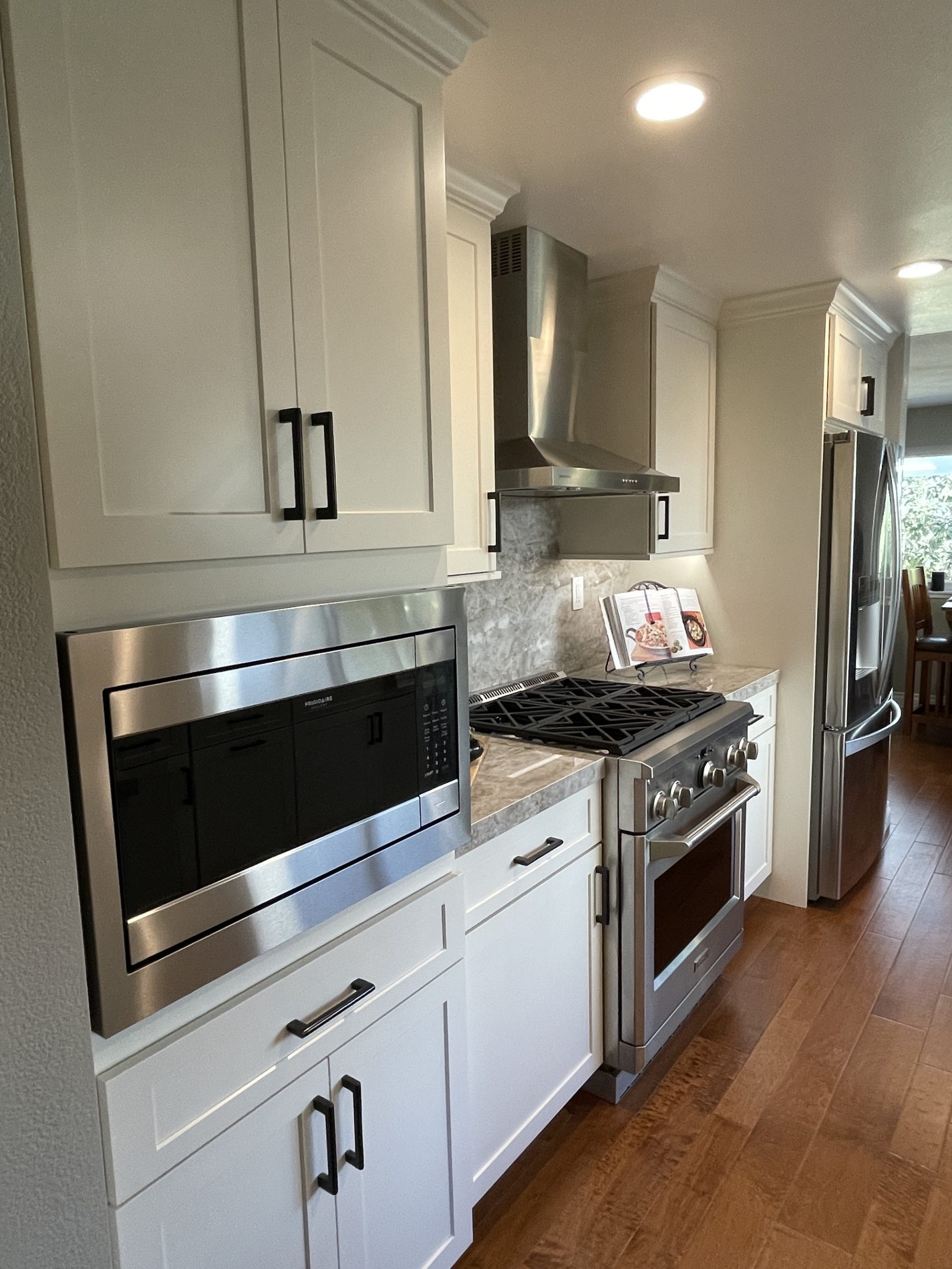 Seneca contemporary galley kitchen with white cabinets, stone counter and backsplash, stainless appliances, wood laminate floor.