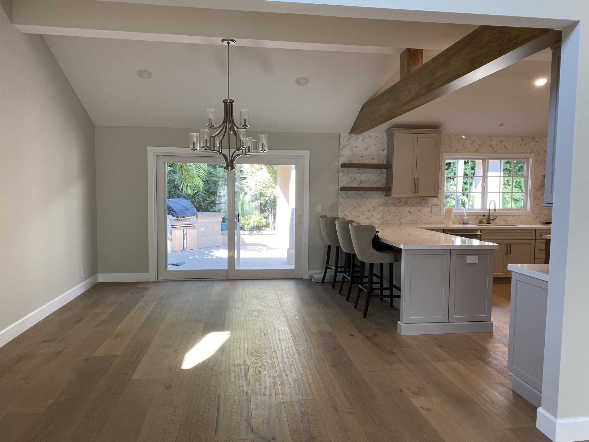 Seneca contemporary gray, cream, farmhouse, open plan kitchen with wood beam, island, shelves, herringbone tile backsplash.
