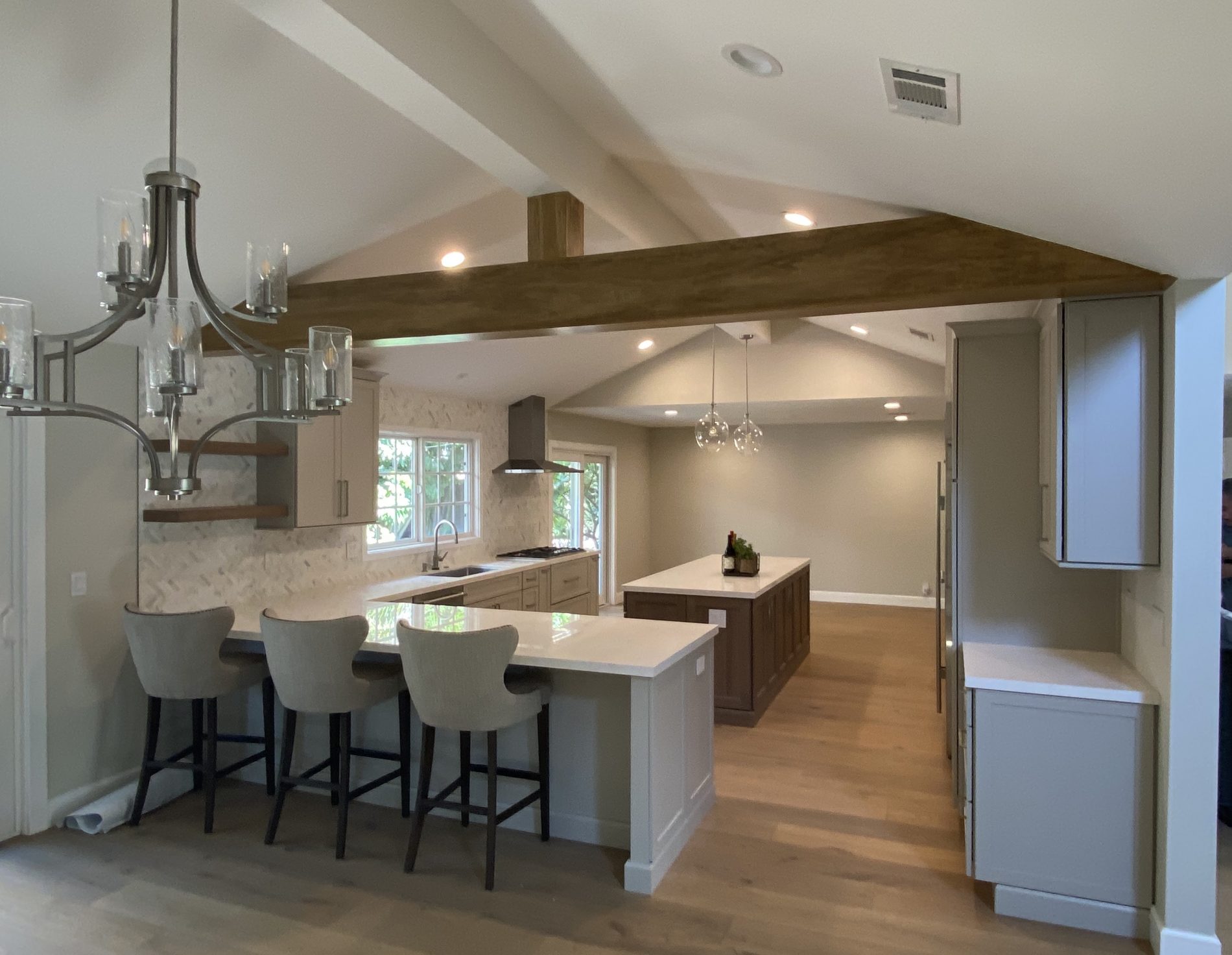 Seneca contemporary gray, cream, farmhouse, open plan kitchen with wood beam, island, shelves, herringbone tile backsplash.